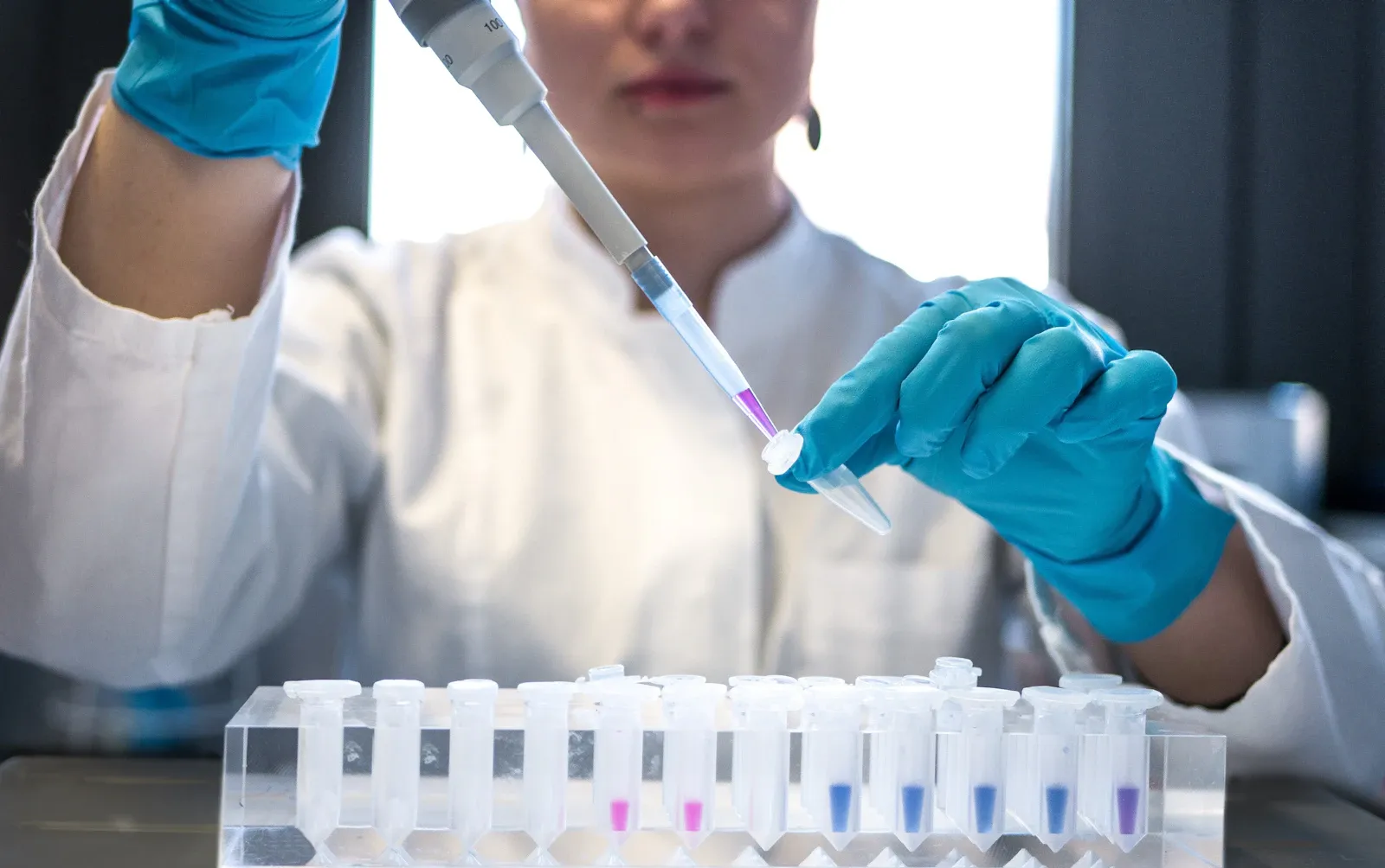Laboratorista con guantes y pipeta preparando muestras de ensayo